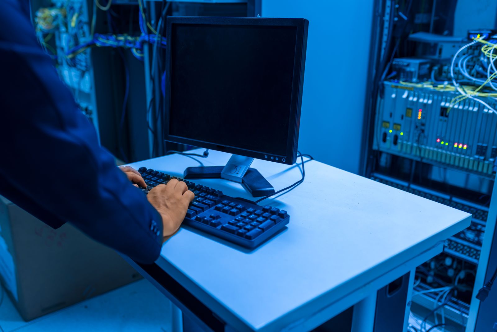 IT technician working at a desk with multiple monitors in a data center server room