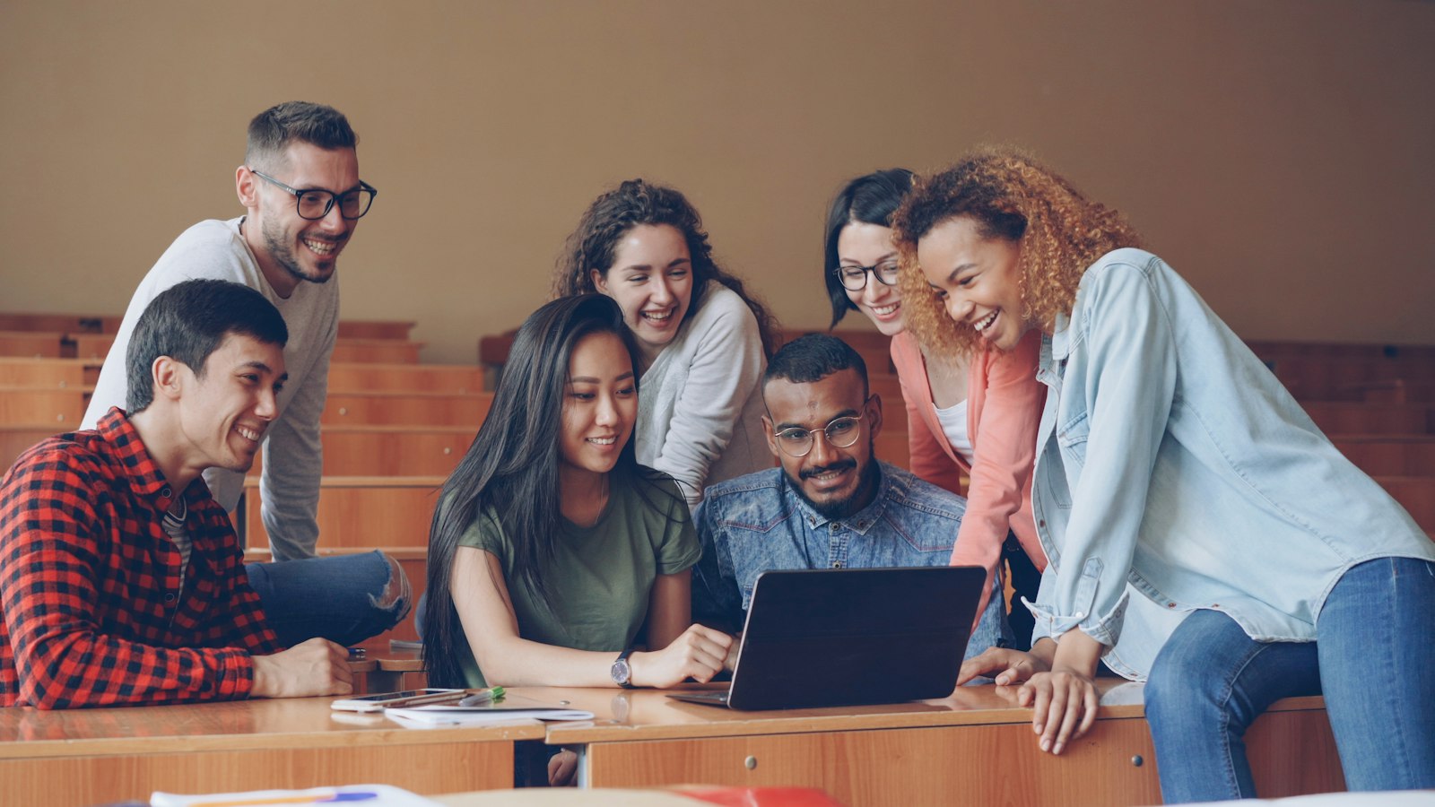 Diverse group of students gathered around a laptop, collaborating and pointing at the screen